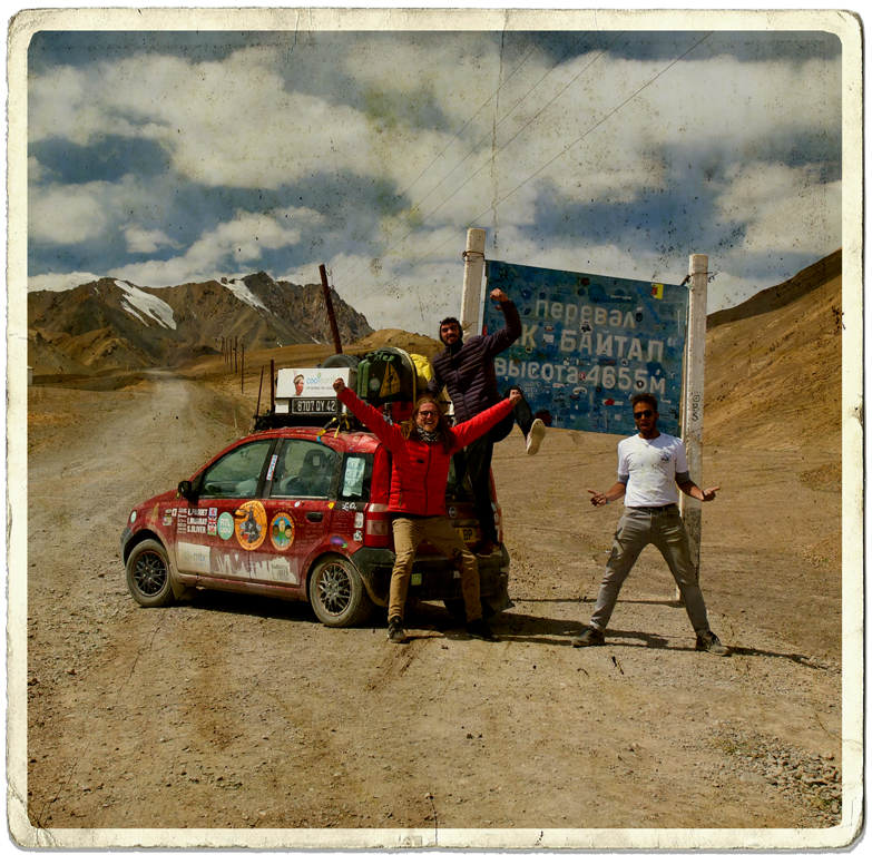 The Mongol Rally 2019 team Bristangolia, including social media travel agency Next Stop Adventures founder and creative strategist, celebrating reaching the highest point of the Pamir highway in front of a road sign and next to their Fiat Panda.