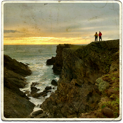 A square old school postcard with 2 hikers, including Next Stop Adventures' social media content strategist Sam Oliver, walking along a coastal path and pointing at the horizon.